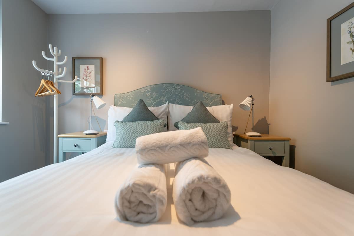 A neatly made bed with rolled towels, a headboard, and two bedside tables with lamps and a framed picture on the wall.