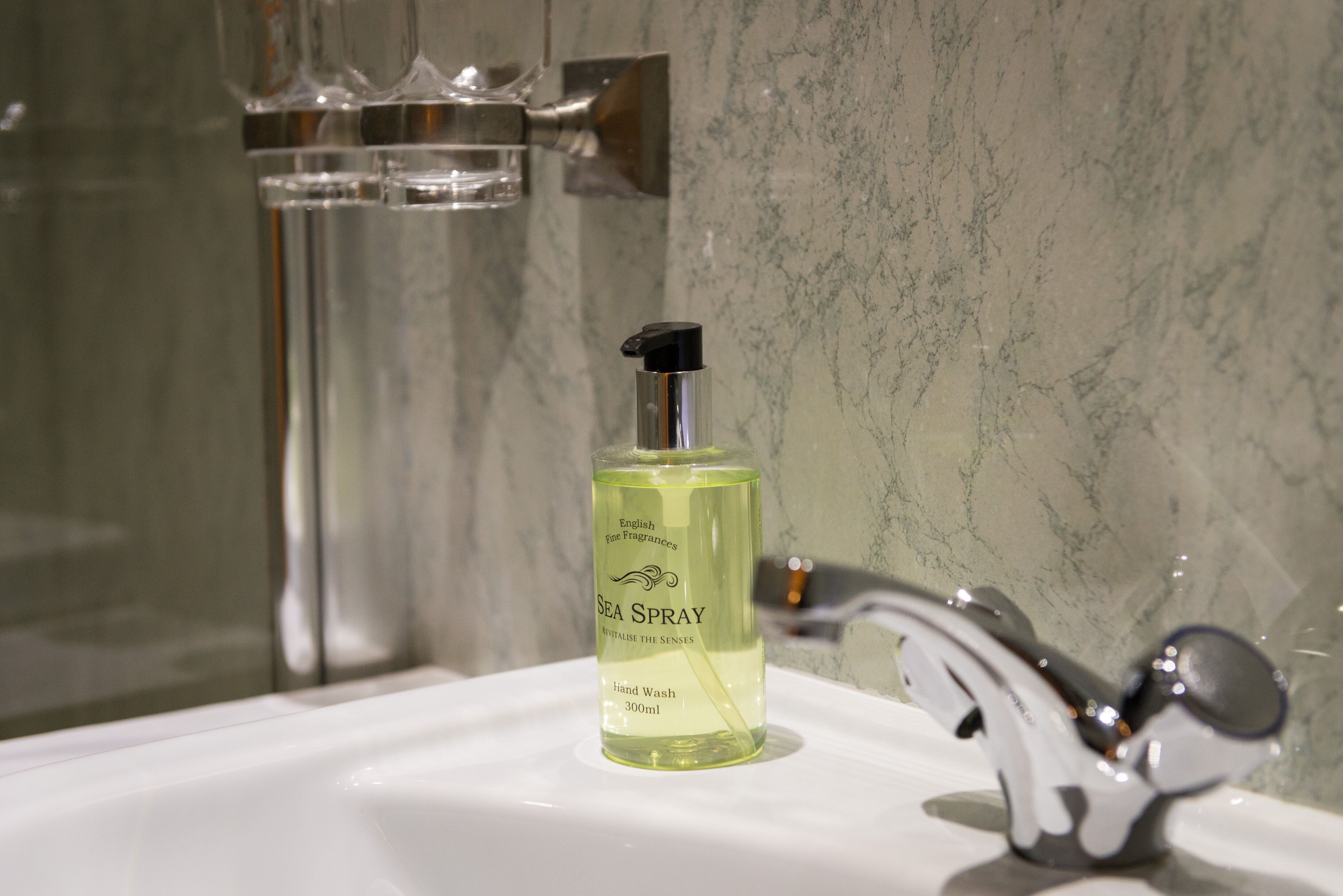 A bathroom with a hand wash bottle labeled "Sea Spray" on a white sink.