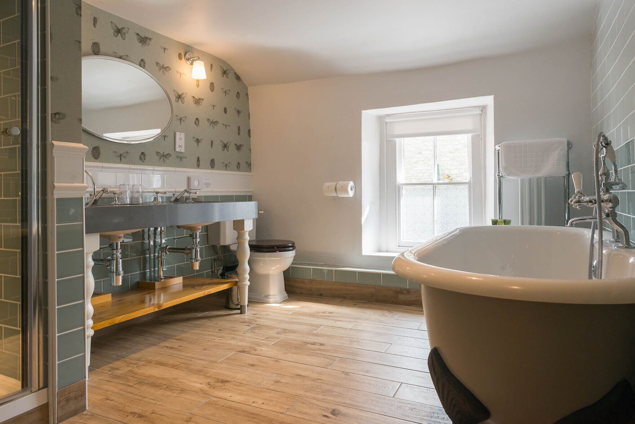 Une salle de bain avec un plancher en bois, une baignoire blanche, des toilettes et un lavabo avec un miroir au-dessus.