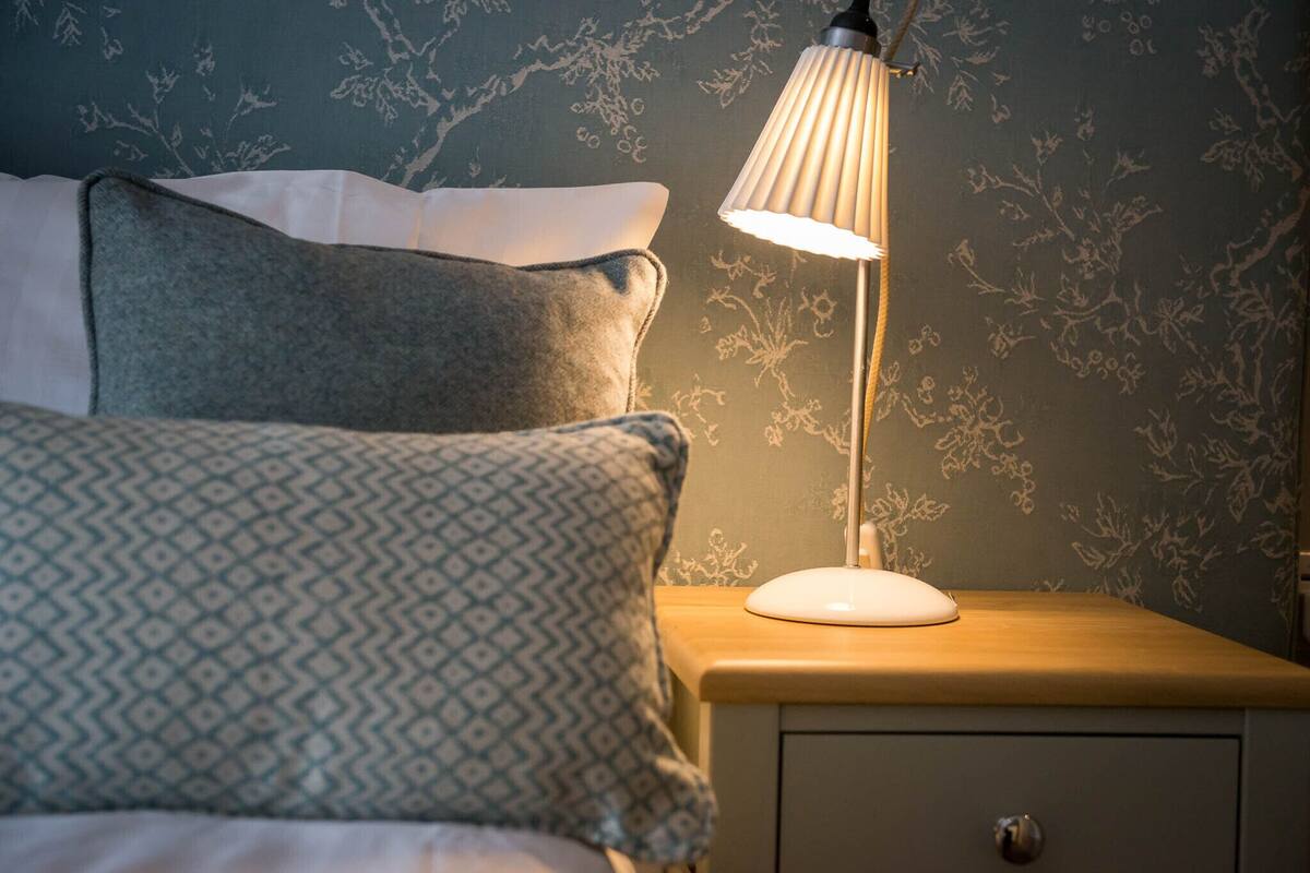 A neatly made bed with patterned pillows, a bedside lamp, and a nightstand with a drawer.