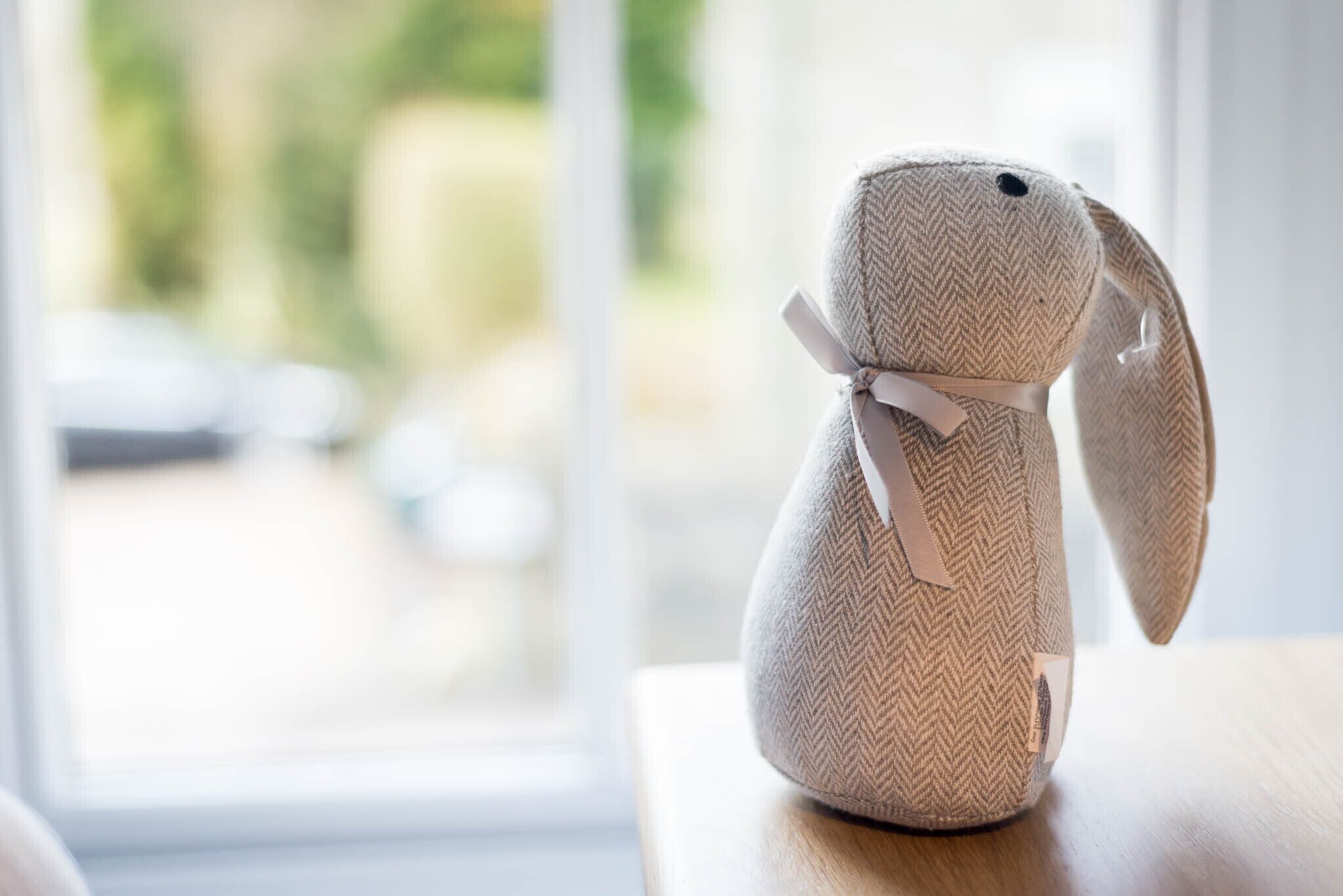 A plush toy with a herringbone pattern and a ribbon on a wooden surface.