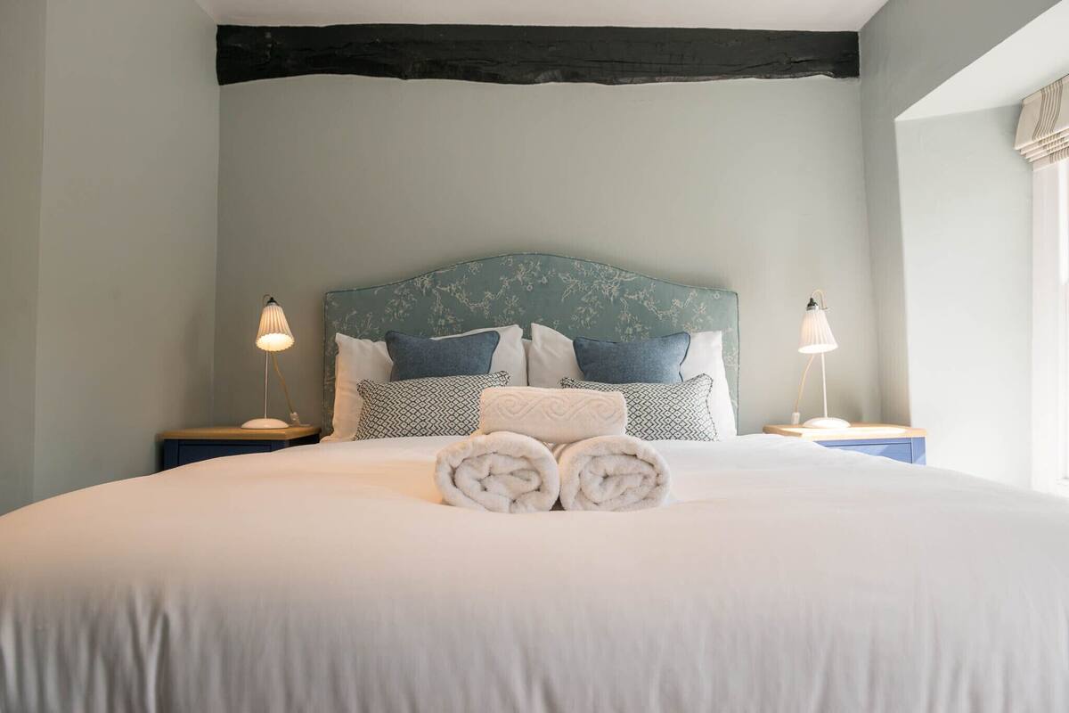 A neatly made bed with rolled towels, a patterned headboard, and bedside lamps.