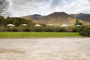 Un espace de stationnement recouvert de gravier, agrémenté d’une rangée de parasols, un terrain herbeux et une chaîne de montagnes en arrière-plan.