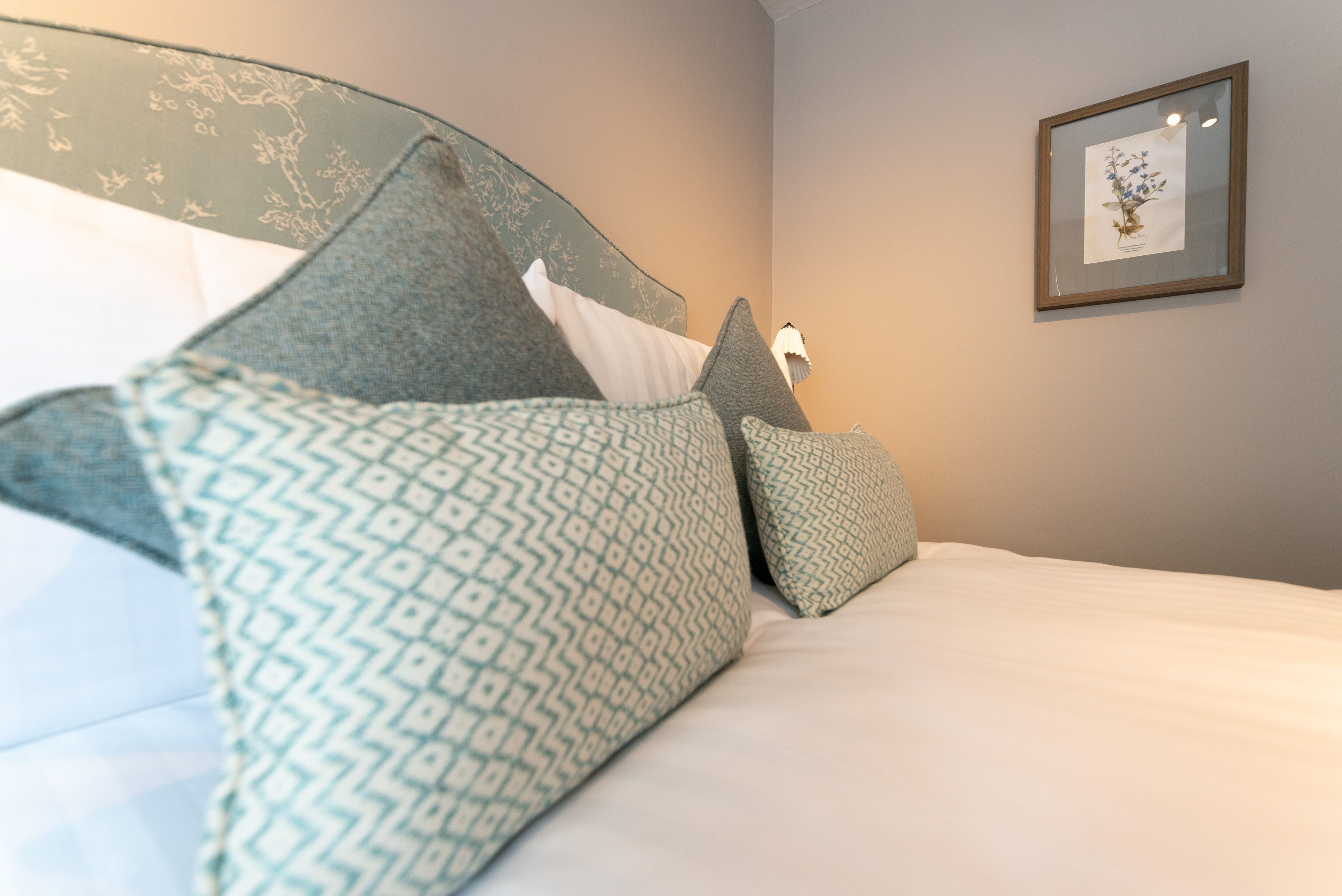 A neatly made bed with patterned pillows and a framed botanical print on the wall.