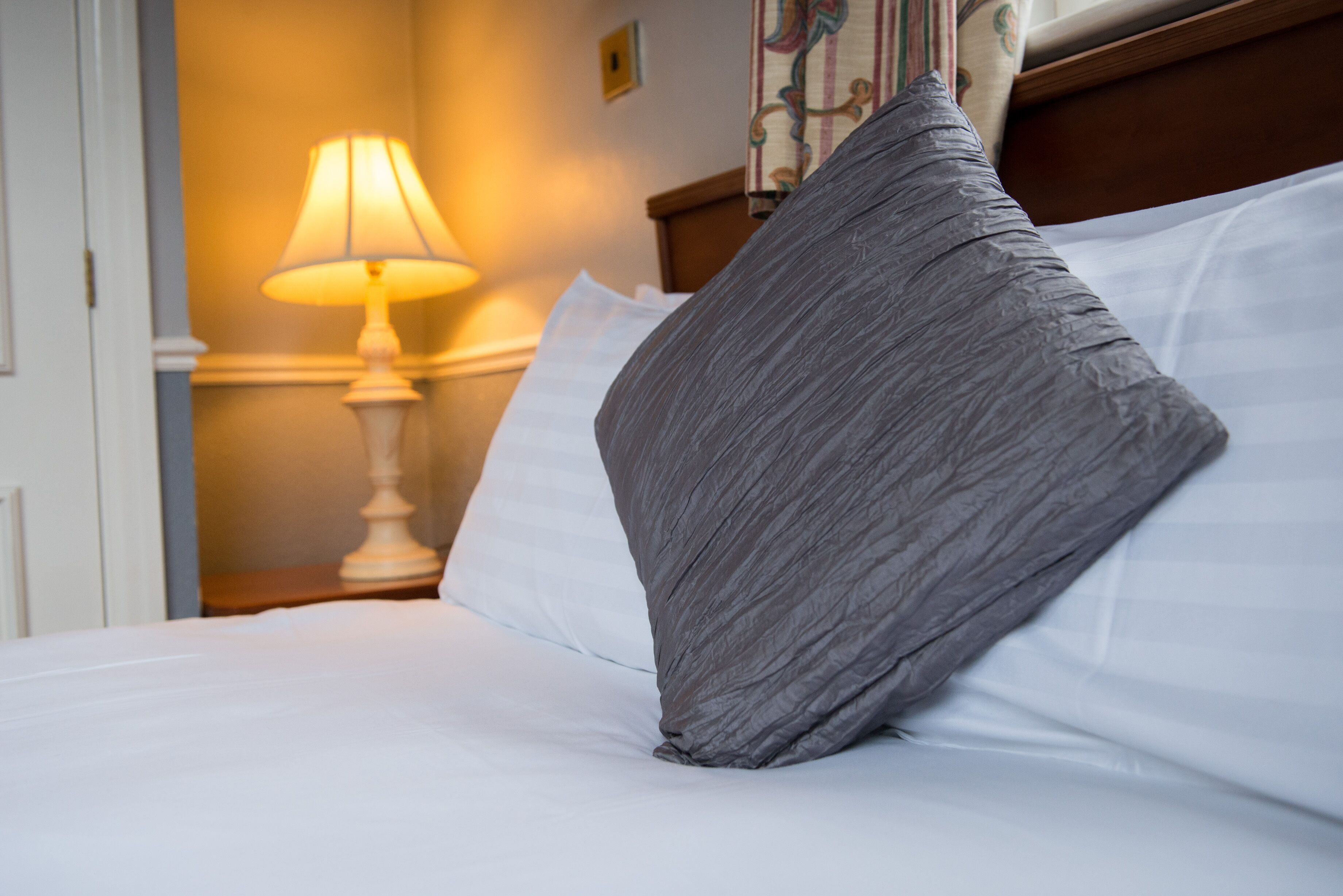 Una cama bien hecha con sábanas blancas y una sola almohada gris.