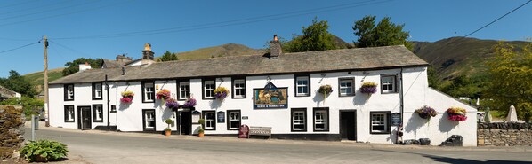 A white building with black-framed windows, a sign reading "Horse & Frier Inn," and flower baskets on the windowsills. - The Horse & Farrier Inn and The Salutation Inn (Keswick)