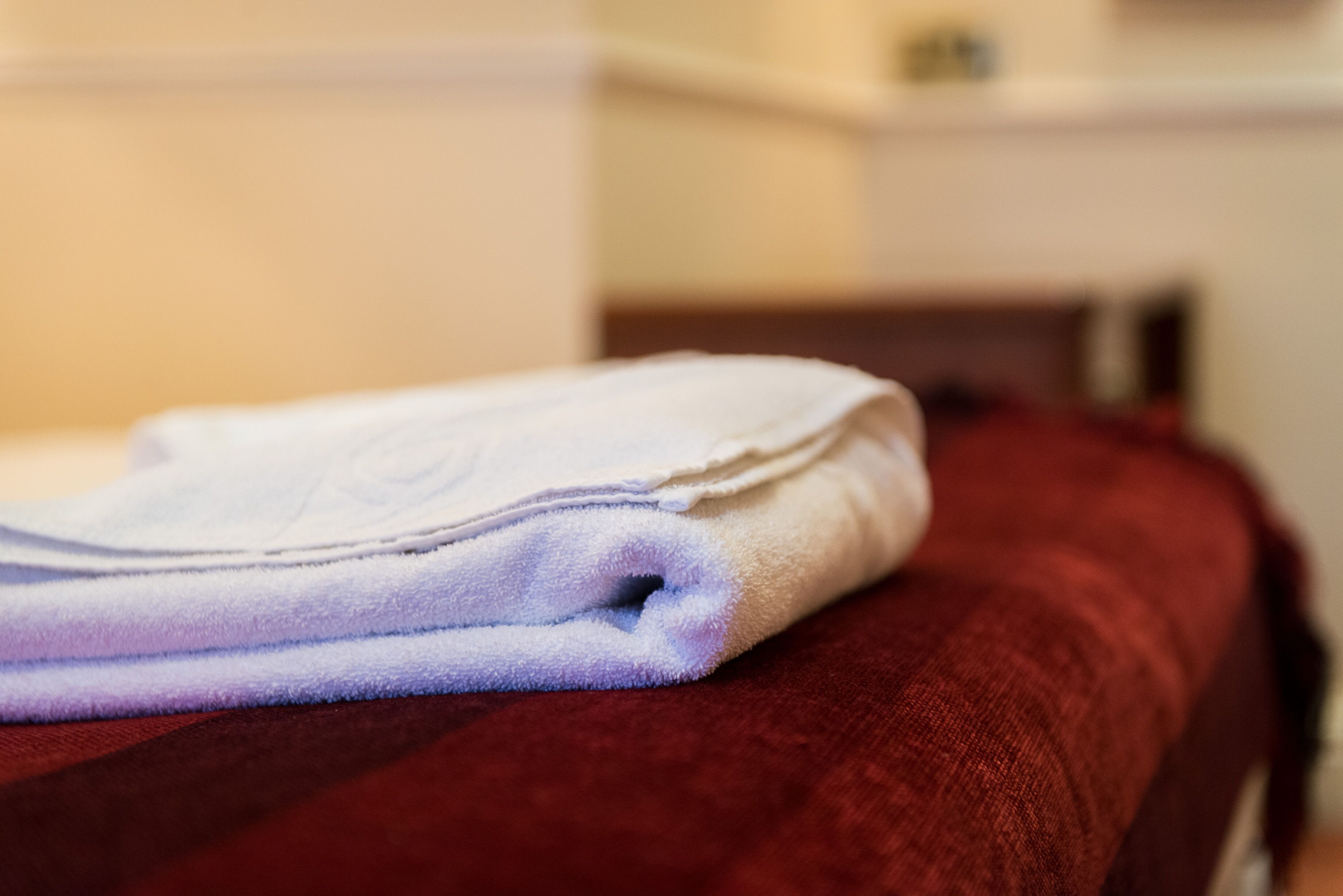 Une serviette blanche, soigneusement pliée, est posée sur un lit rouge.