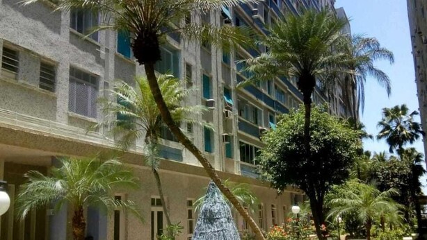 Un patio con palmeras, un banco y un edificio de varios pisos y balcones.