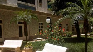 Un área con mesas al aire libre, con dos bancos, una planta en maceta y un edificio de fachada de piedra.
