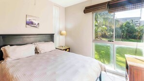 A bedroom with a bed, a nightstand, a lamp, a window with a view of greenery, and a wall-mounted picture. - La Ballito Self Catering Apartment (Ballito)