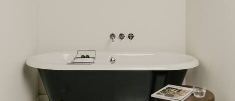 A bathroom with a freestanding bathtub, wooden beams on the ceiling, and a small wooden stool with a magazine and glass of water.