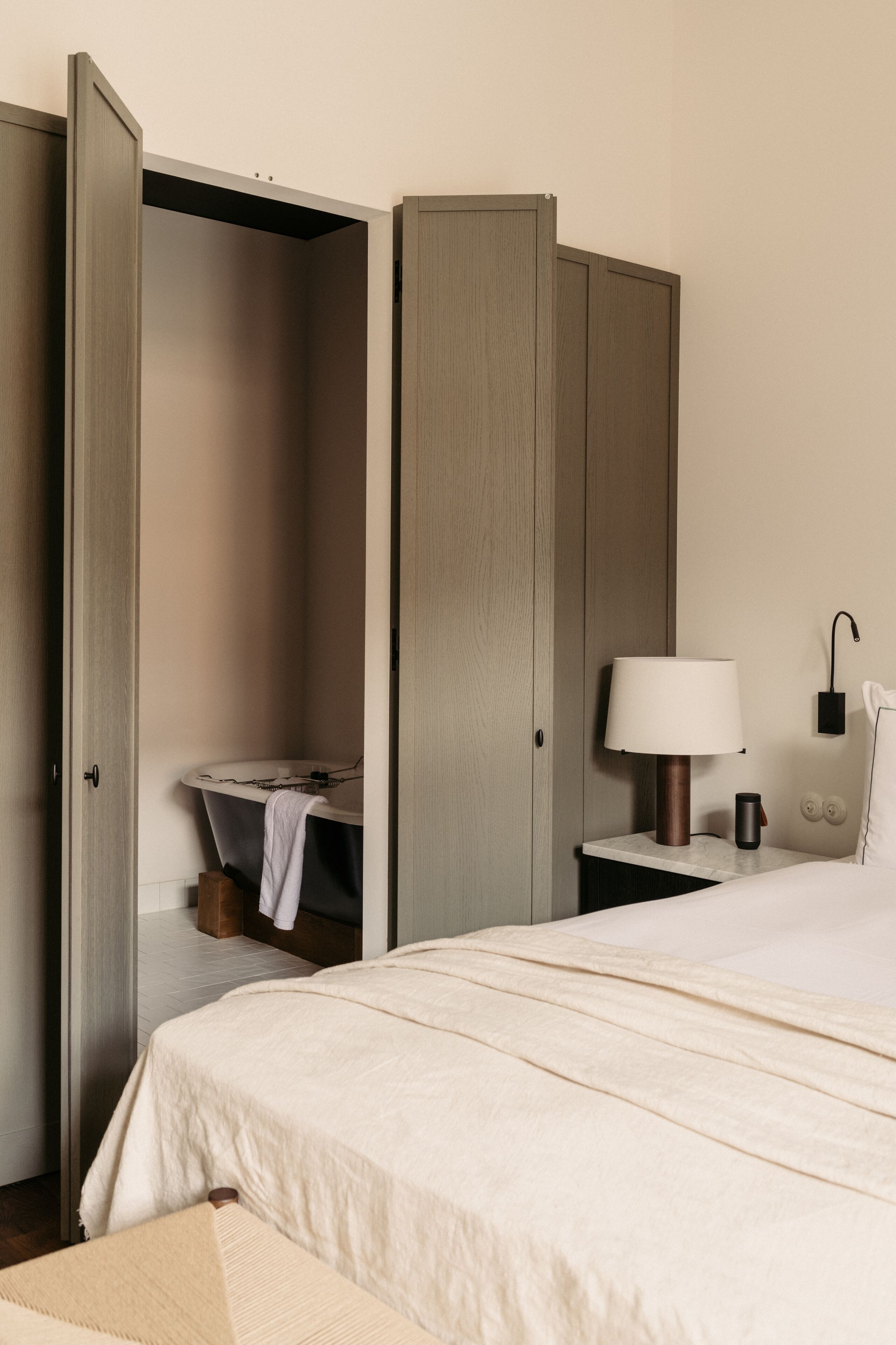 Una habitación de hotel con cama, mesita de noche con lámpara, mesita auxiliar y armario.