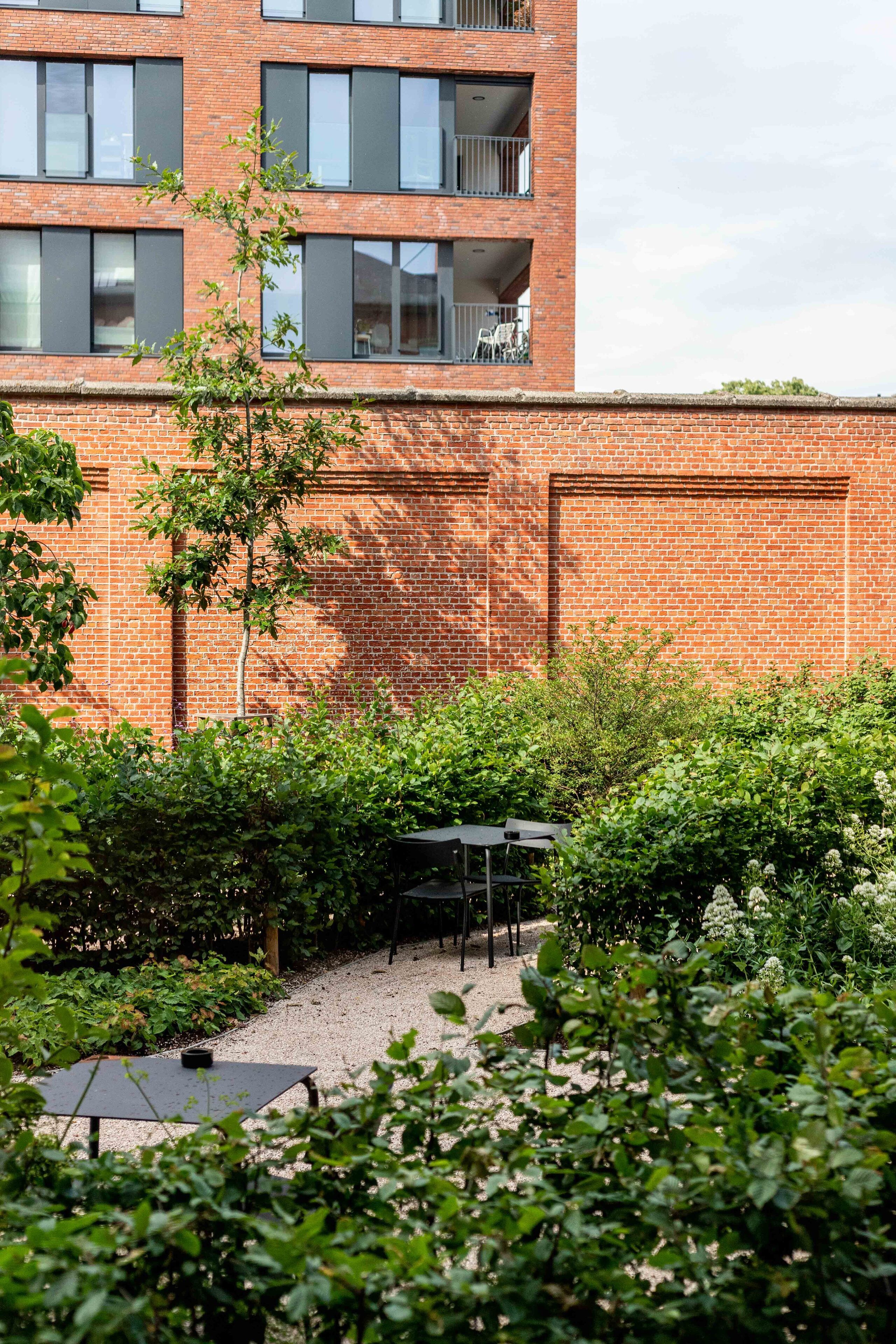 A courtyard with a brick building, a small tree, and a table with chairs.