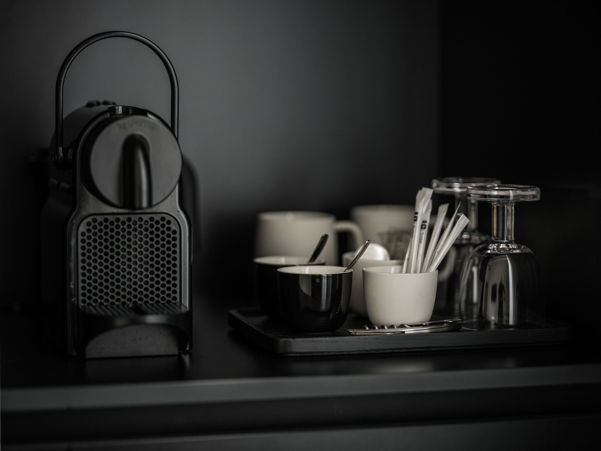 A kitchenette with a coffee maker, cups, and a tray.