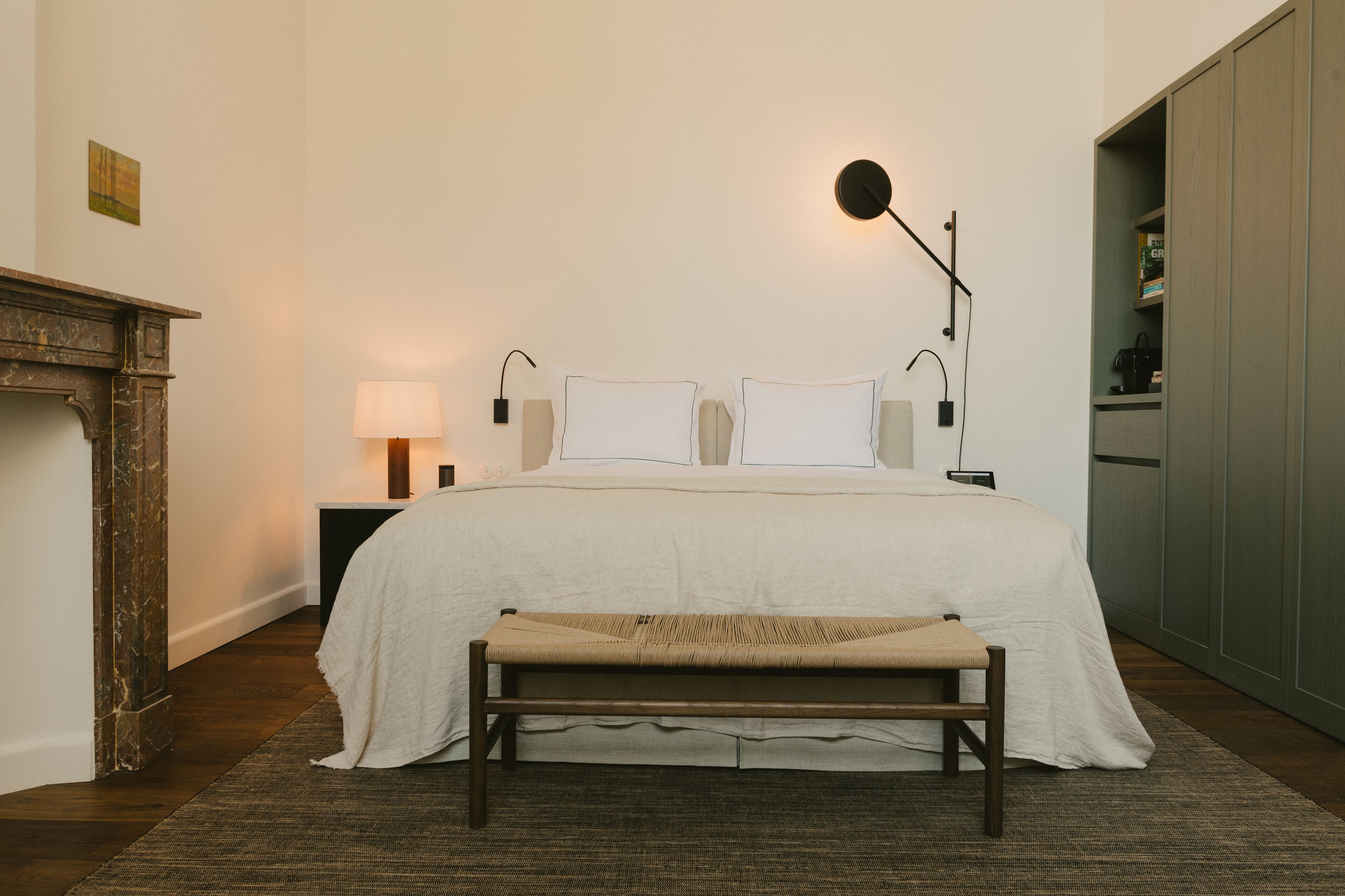 A neatly arranged bedroom with a large bed, bedside lamps, a bench, and a wardrobe.