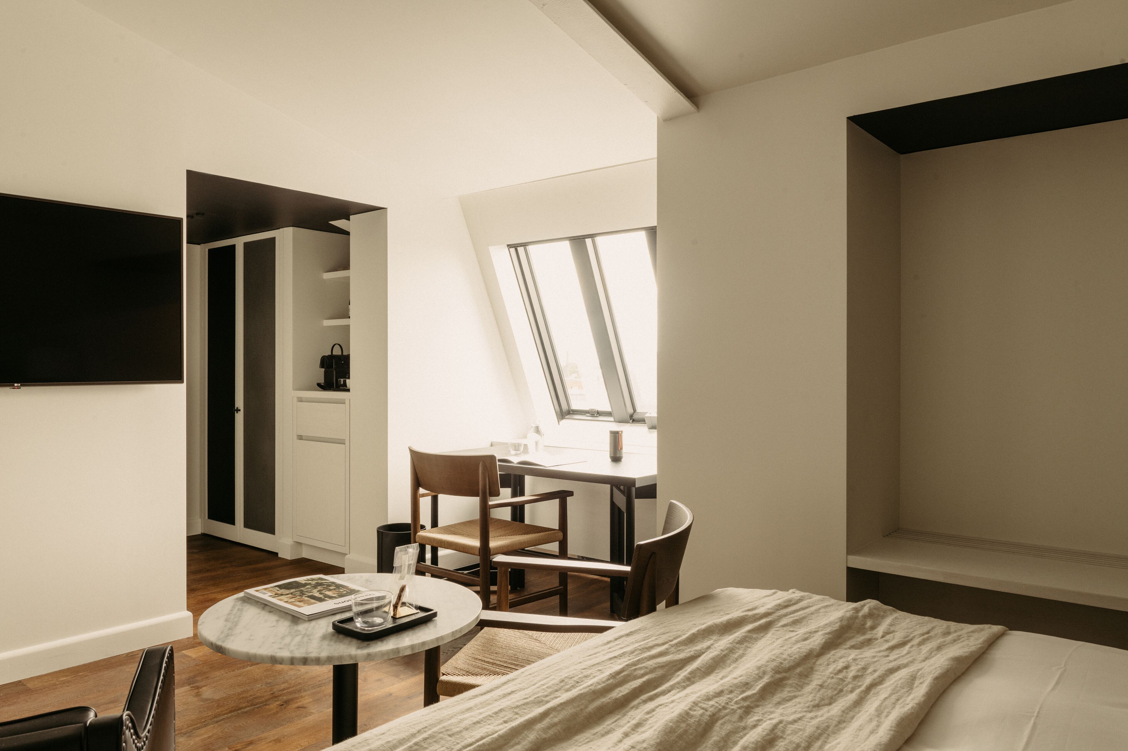 A bedroom with a bed, a desk, and a chair. There is a window providing natural light.