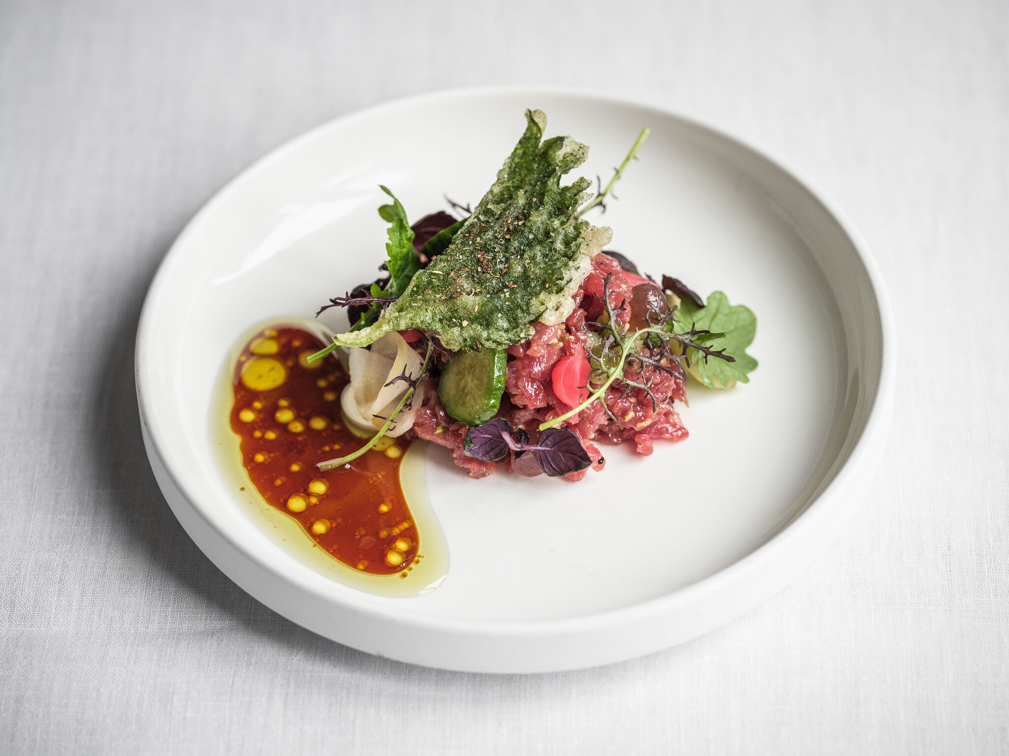 Un plato blanco con guiso de carne cruda, verduras y salsa.