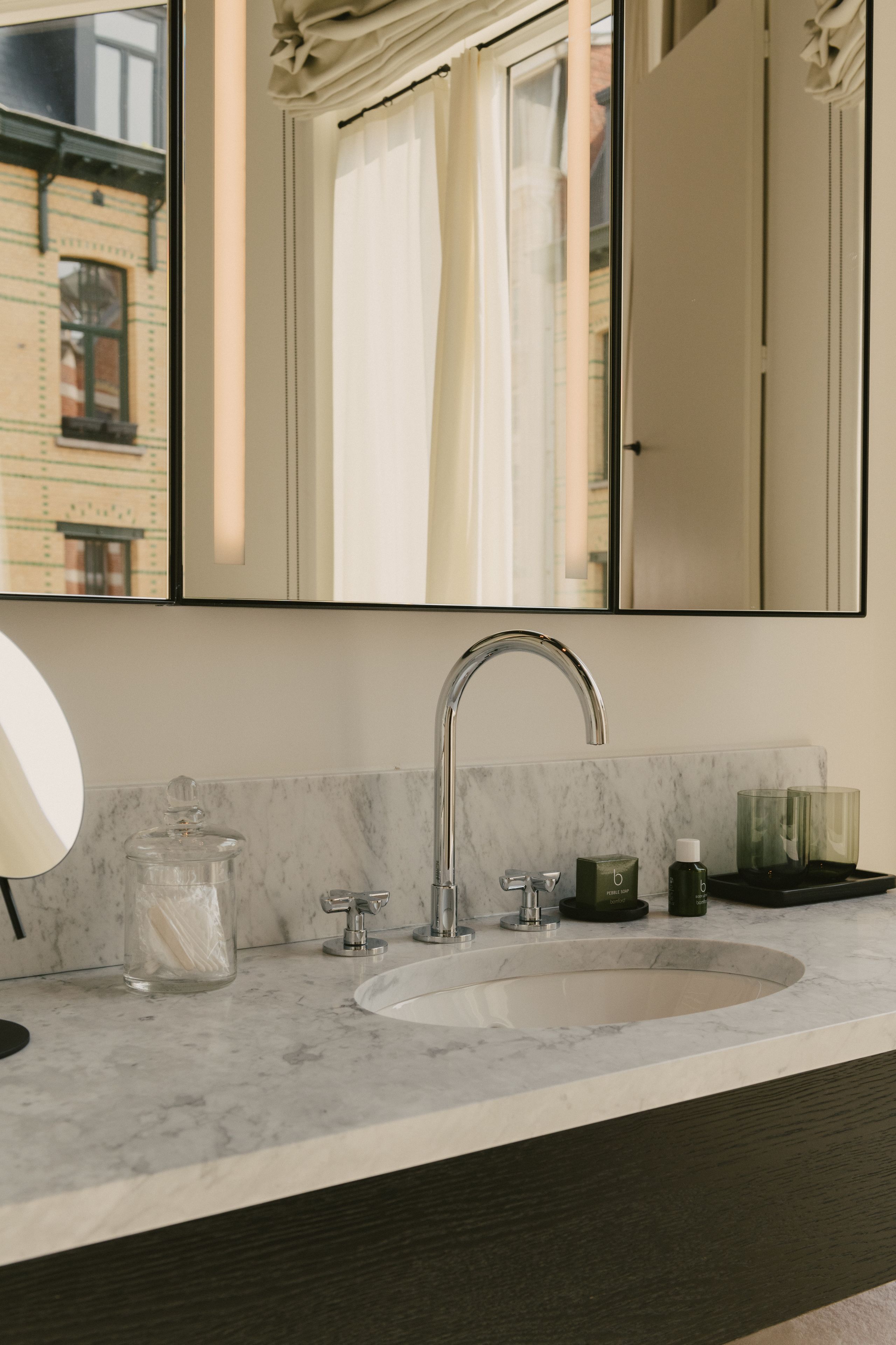 Un baño moderno con un espejo grande, un lavamanos y una ventana con cortinas.