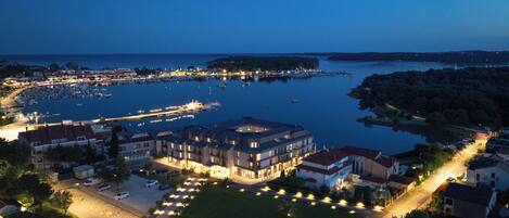 A coastal town at dusk with a marina, residential buildings, and a well-lit parking area.
