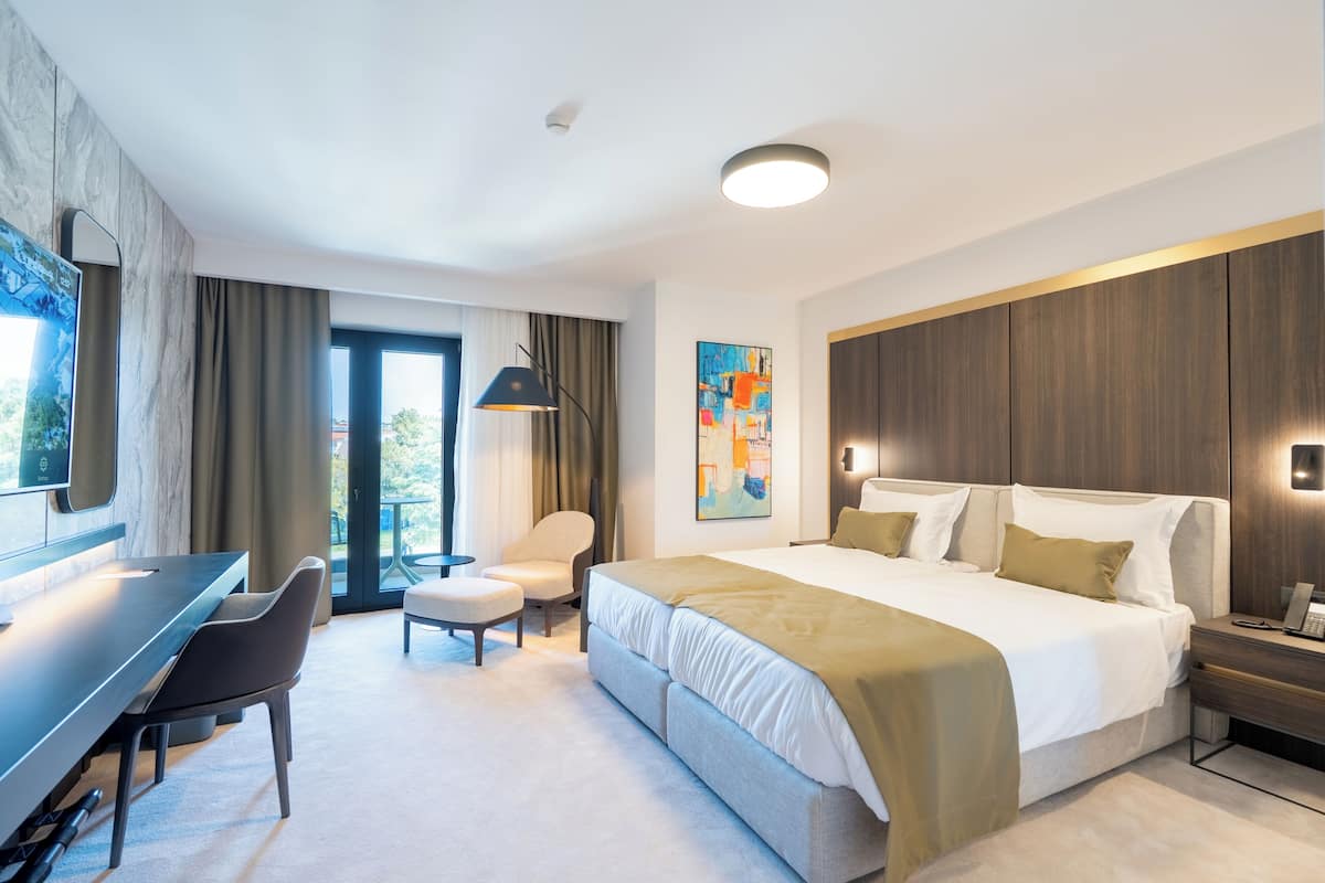 A modern hotel room with a bed, desk, chair, and artwork on the wall.