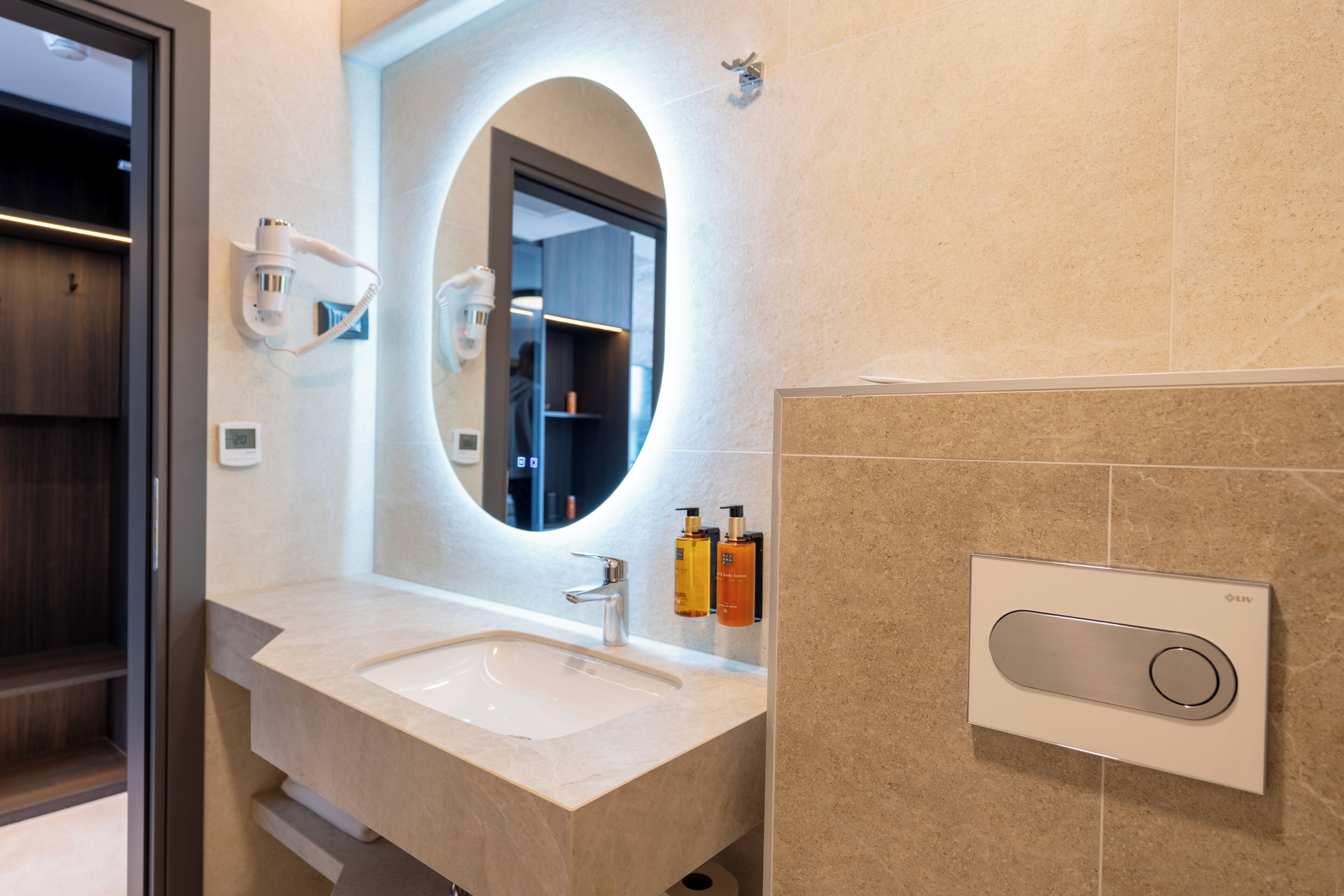 A modern bathroom with a large oval mirror, a sink, and a wall-mounted hairdryer.