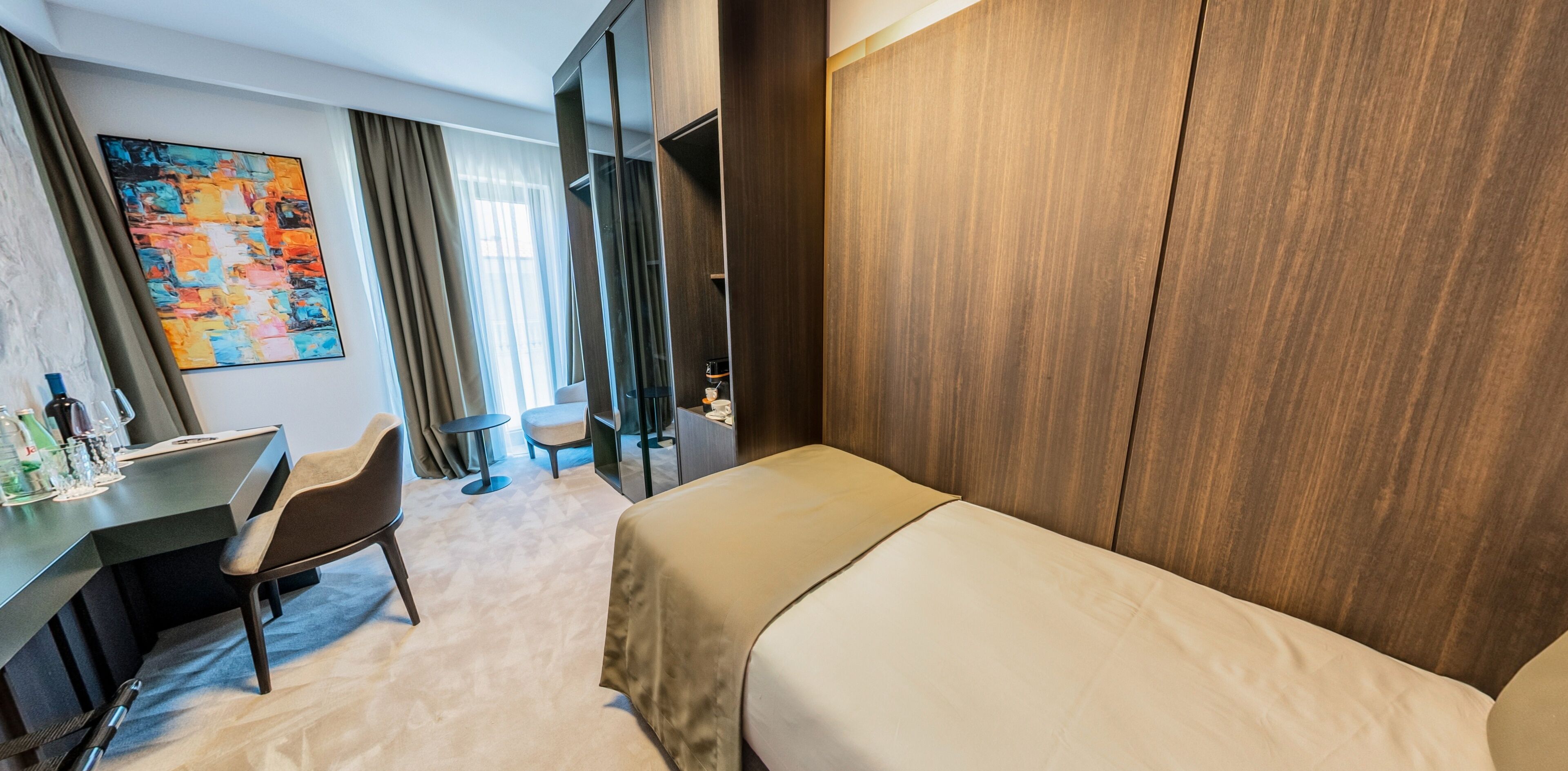 Et hotelværelse med seng, skrivebord, stol, lille bord og et billede på væggen.