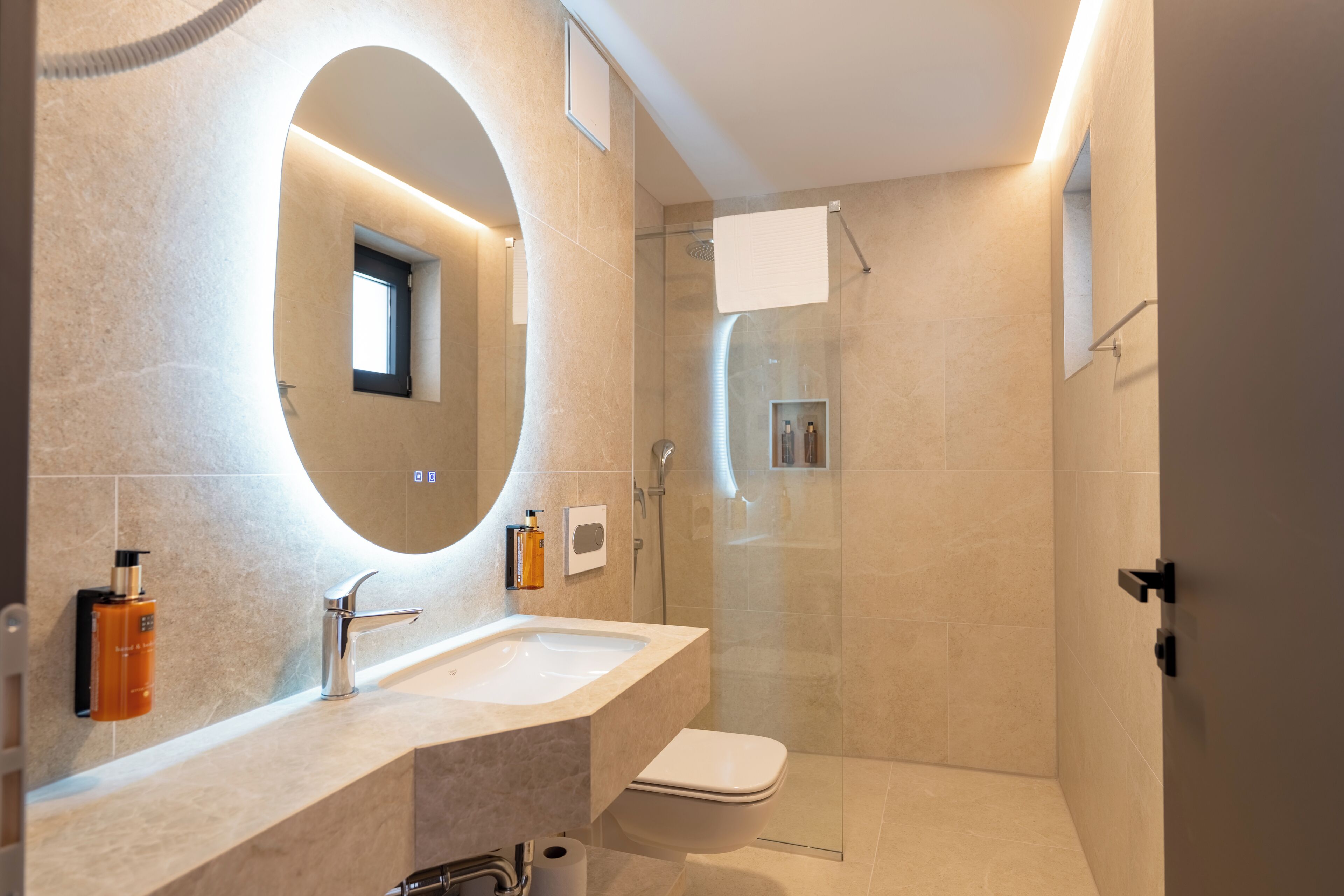 Une salle de bain moderne avec un grand miroir ovale, un lavabo, des toilettes et un espace douche.
