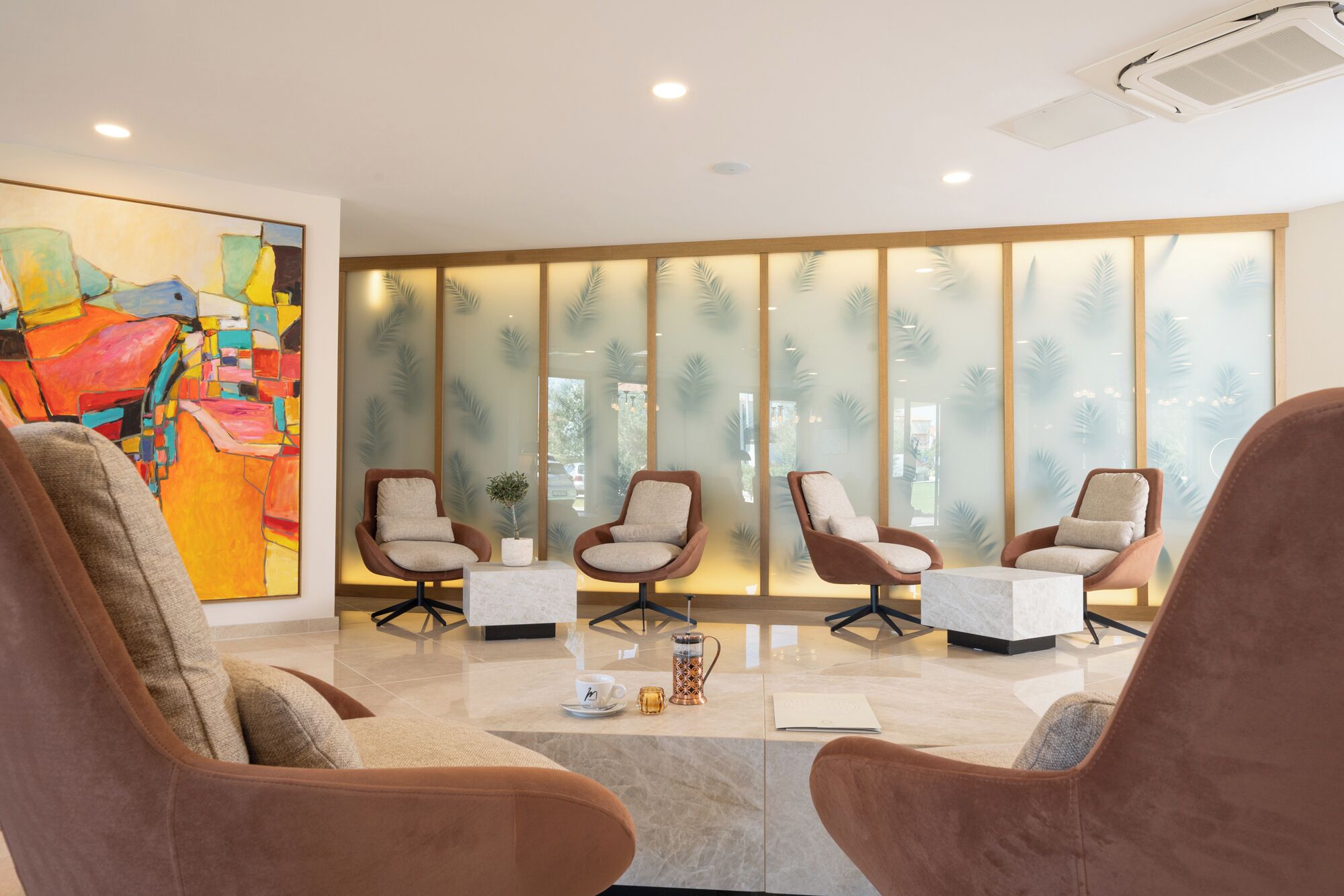 Een moderne lobby met drie bruine fauteuils, een bijzettafeltje en een groot abstract schilderij aan de linkerkant.
