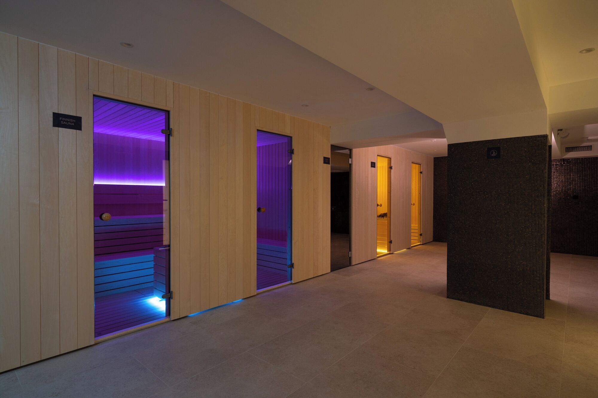 Un pasillo con paredes y puertas de madera que dan a habitaciones, algunas con iluminación púrpura.