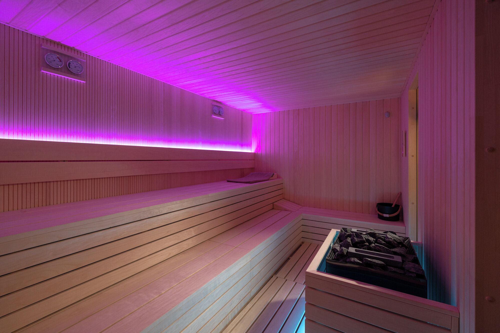 Una sauna amb bancs de fusta i un banc amb un estri, un cubell i un safata de pedres.