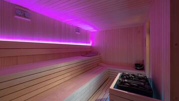 Eine Sauna mit Holzbänken und einer Liege mit Matte, einem Eimer und einem Tablett mit Steinen.