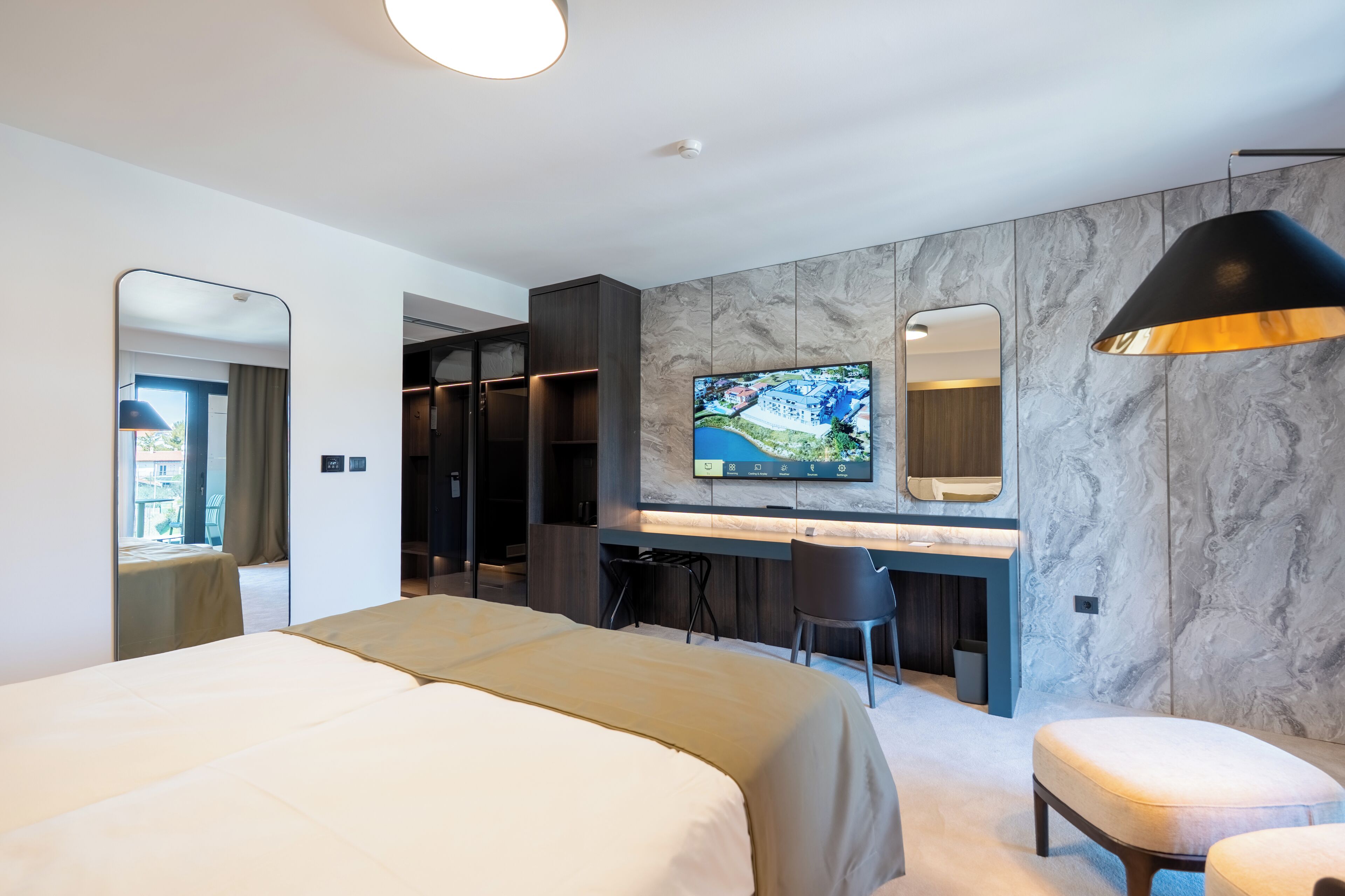 A modern hotel room with a bed, a desk, a TV, and a large mirror.