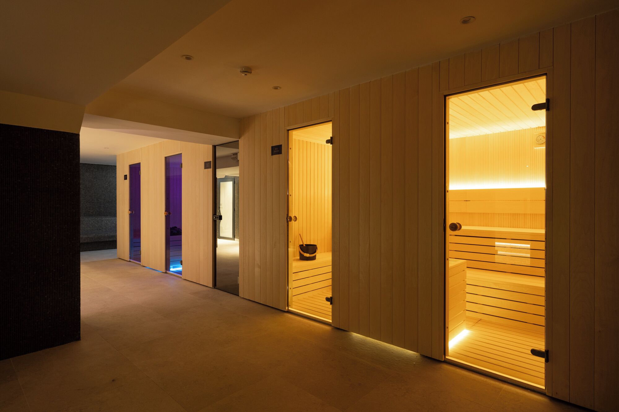 A hallway with wooden doors leading to rooms, a tiled floor, and recessed ceiling lighting.