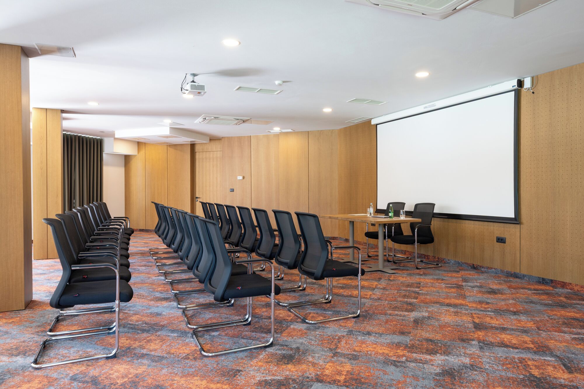 A conference room with rows of chairs, a projector screen, and a carpeted floor.