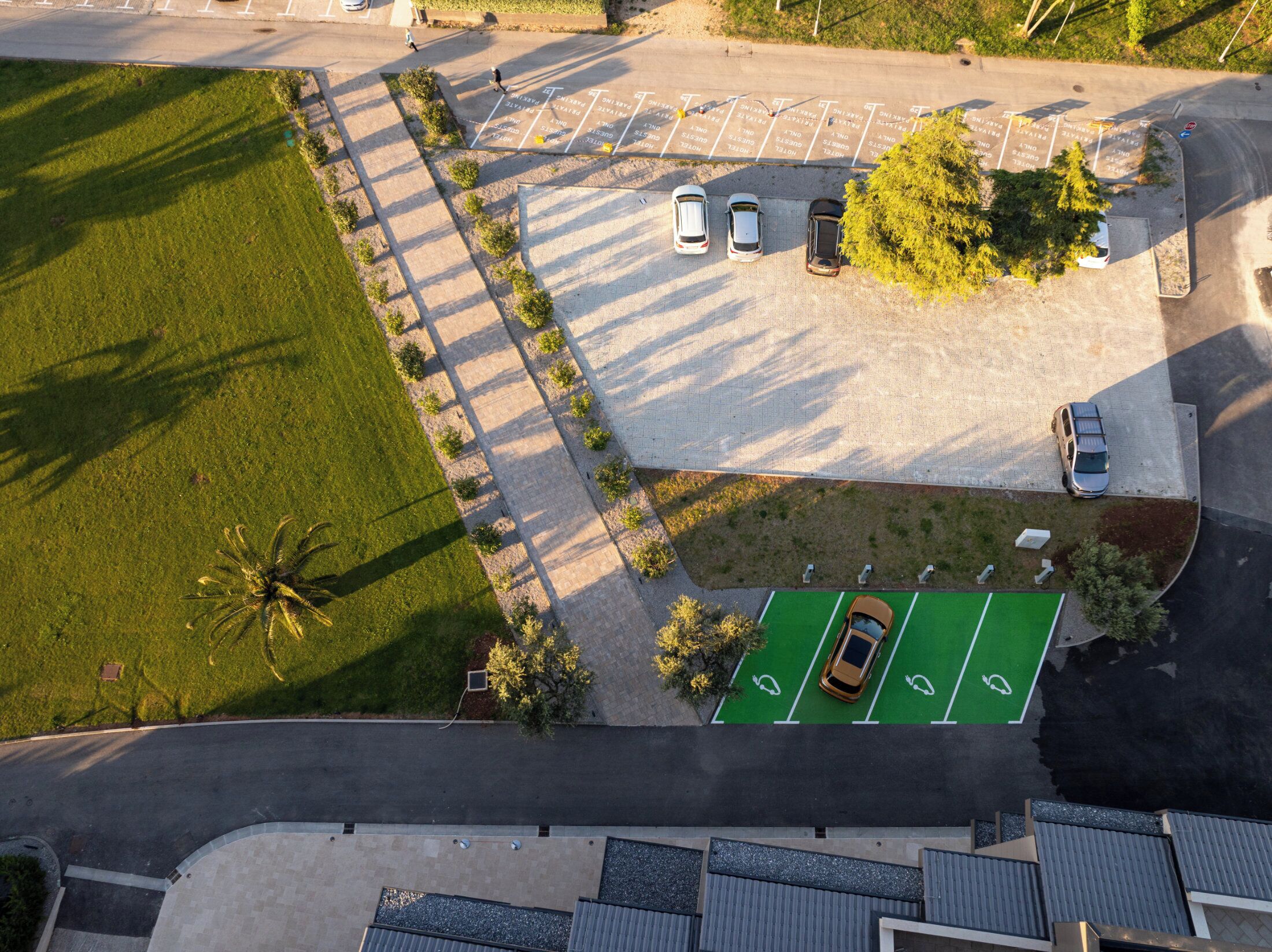 Vista aèria d'un pàrquing amb places delimitades, un camp esportiu verd i vegetació als voltants.