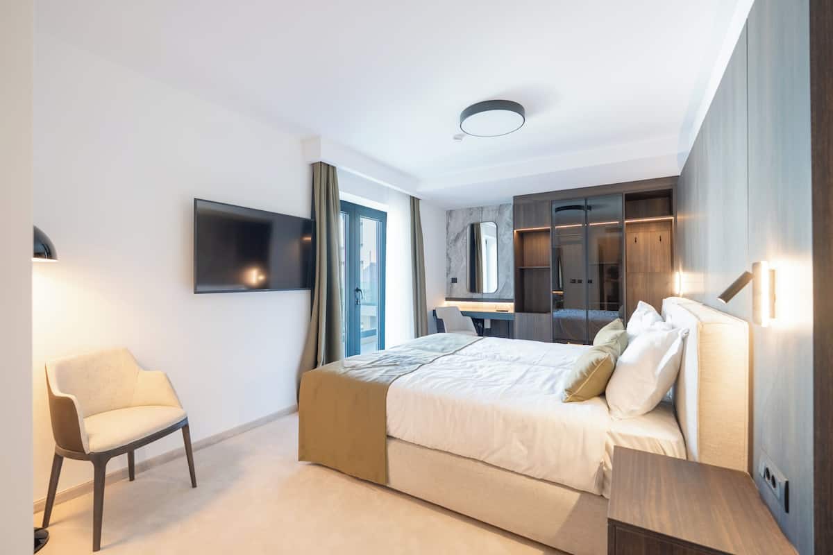 A modern hotel room with a bed, a desk, a chair, a TV, and a bathroom.
