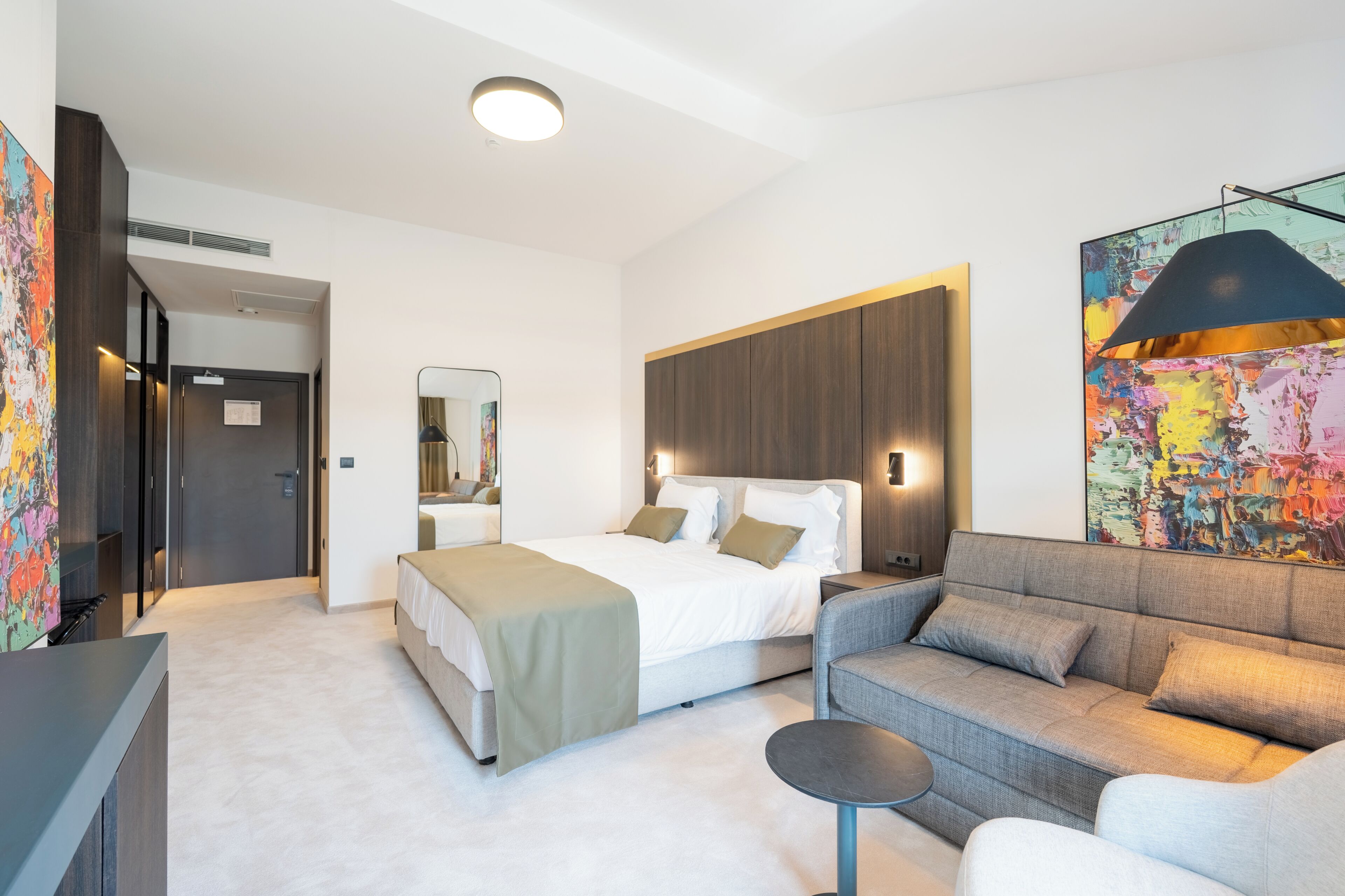 Ein modernes Hotelzimmer mit Bett, Sofa und einem großen abstrakten Gemälde.