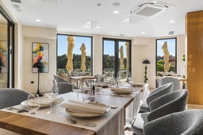 A dining area with tables set for service, large windows with umbrellas, and a view of greenery. - Visula Hotel & Spa - New Opening 2026 (Medulin)
