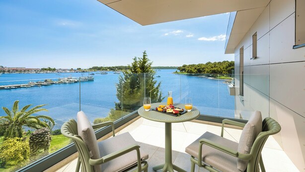 Un balcón con una mesa dispuesta para dos personas, con vistas a un puerto deportivo y al agua.
