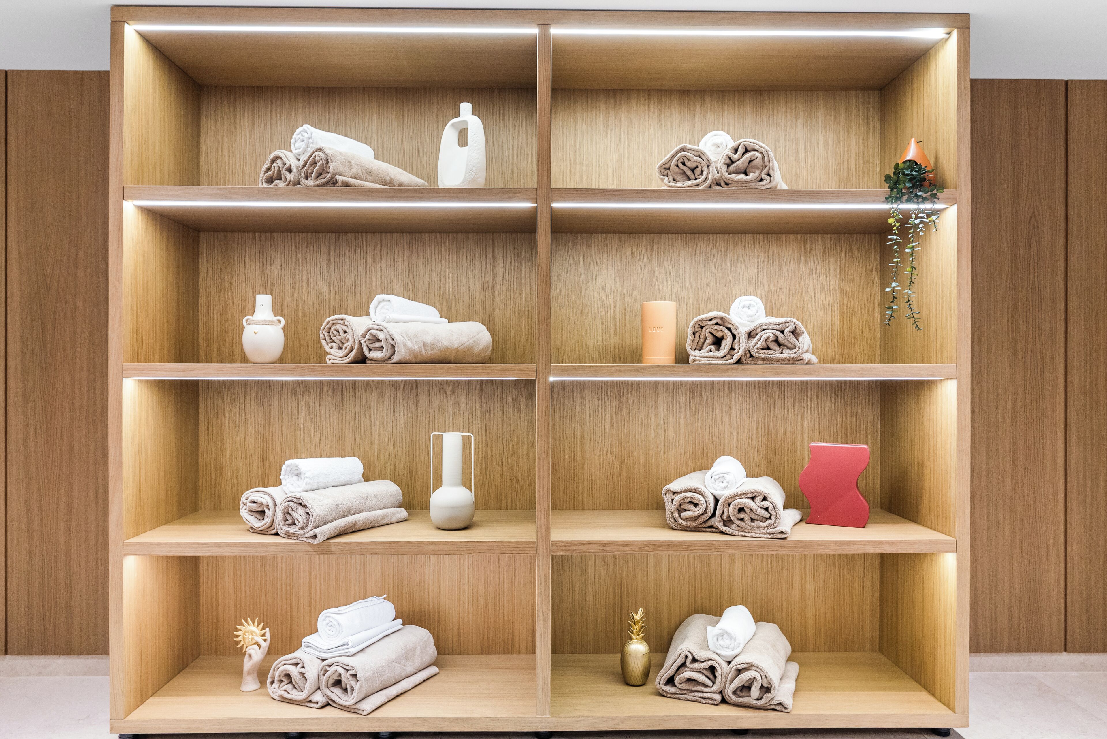 A wooden shelving unit with neatly folded towels, a white vase, and a small plant.