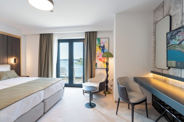 Una habitación de hotel moderna con una cama grande, un escritorio, una silla, una lámpara de escritorio y un cuadro en la pared.