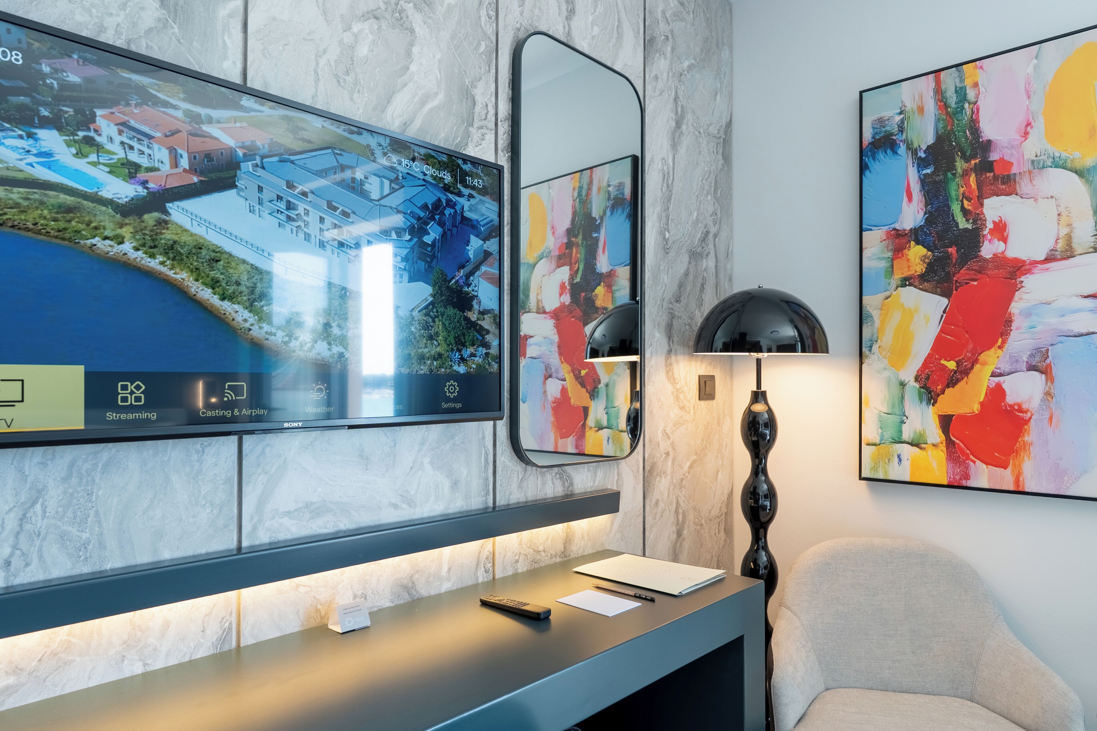 A modern hotel reception area with a large digital display, a desk with a lamp, and abstract art on the wall.