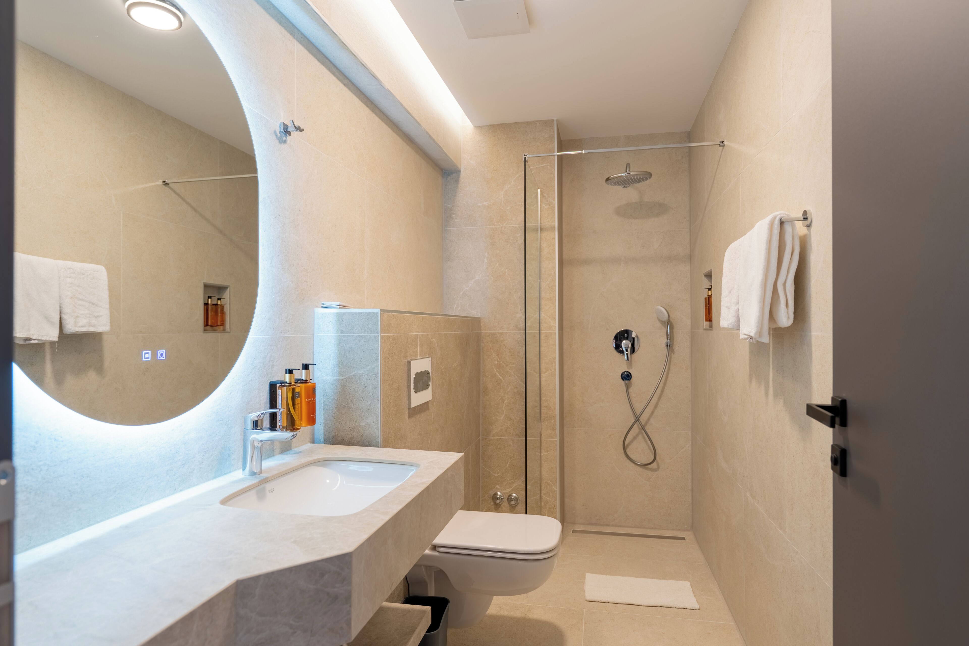 A modern bathroom with a curved mirror, a sink, a toilet, and a glass-enclosed shower.