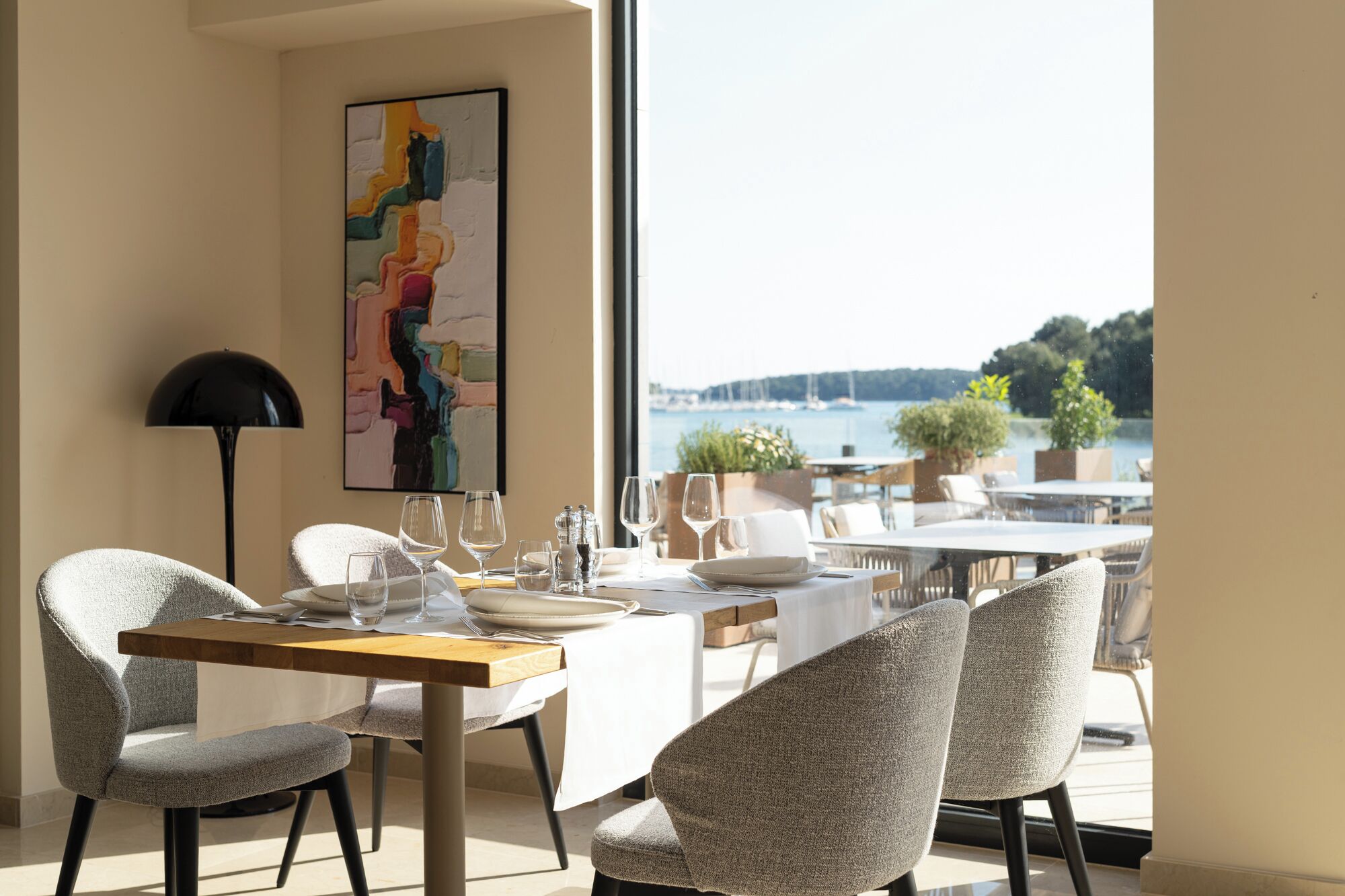 A dining area with a table set for two, a modern lamp, and a view of the water.