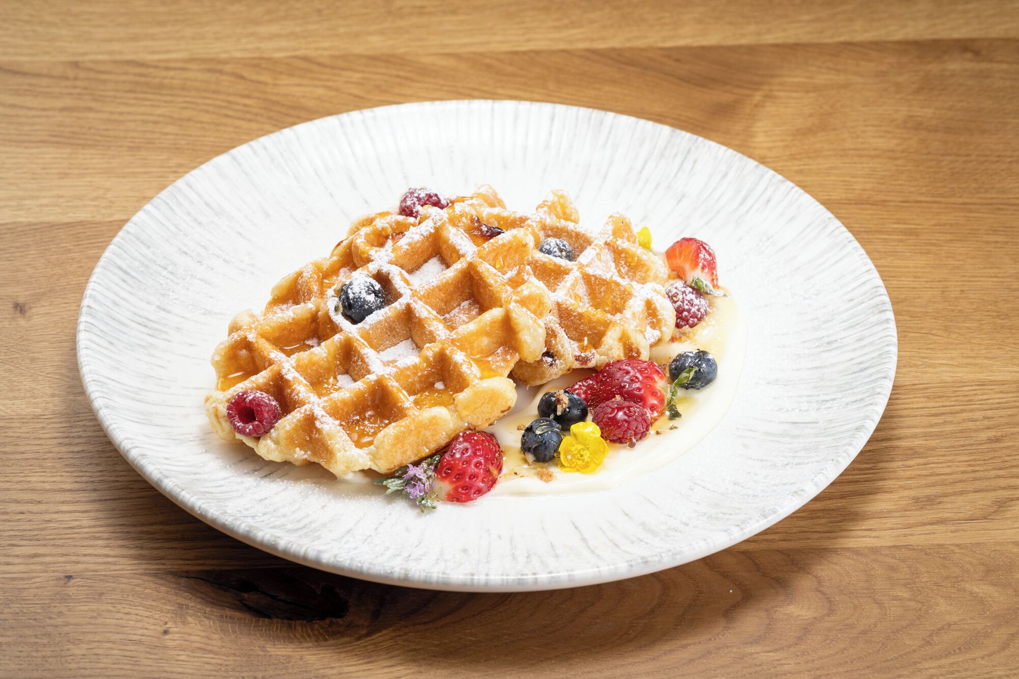 Een bord met wafels, bessen en siroop op een houten tafel.