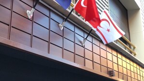 Fachada de un edificio con barandilla metálica y dos banderas, una azul con estrellas y otra rojo y blanco con media luna y estrella.