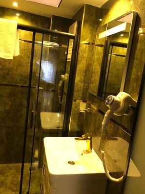 A modern bathroom with a glass-enclosed shower, a white sink with a handheld showerhead, and a mirror with integrated lighting.