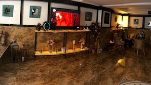 Un vestíbulo espacioso con suelo de mármol, un televisor de pantalla plana grande, una recepción y una zona de estar con sillas y una mesa.