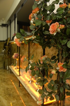 A row of artificial rose plants with a marble floor and a brass lamp in the background.
