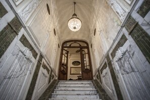 Un magnifique escalier en marbre, avec des marches de marbre et des portes en bois richement décorées, menant à un plafond haut orné d’un lustre en cristal.